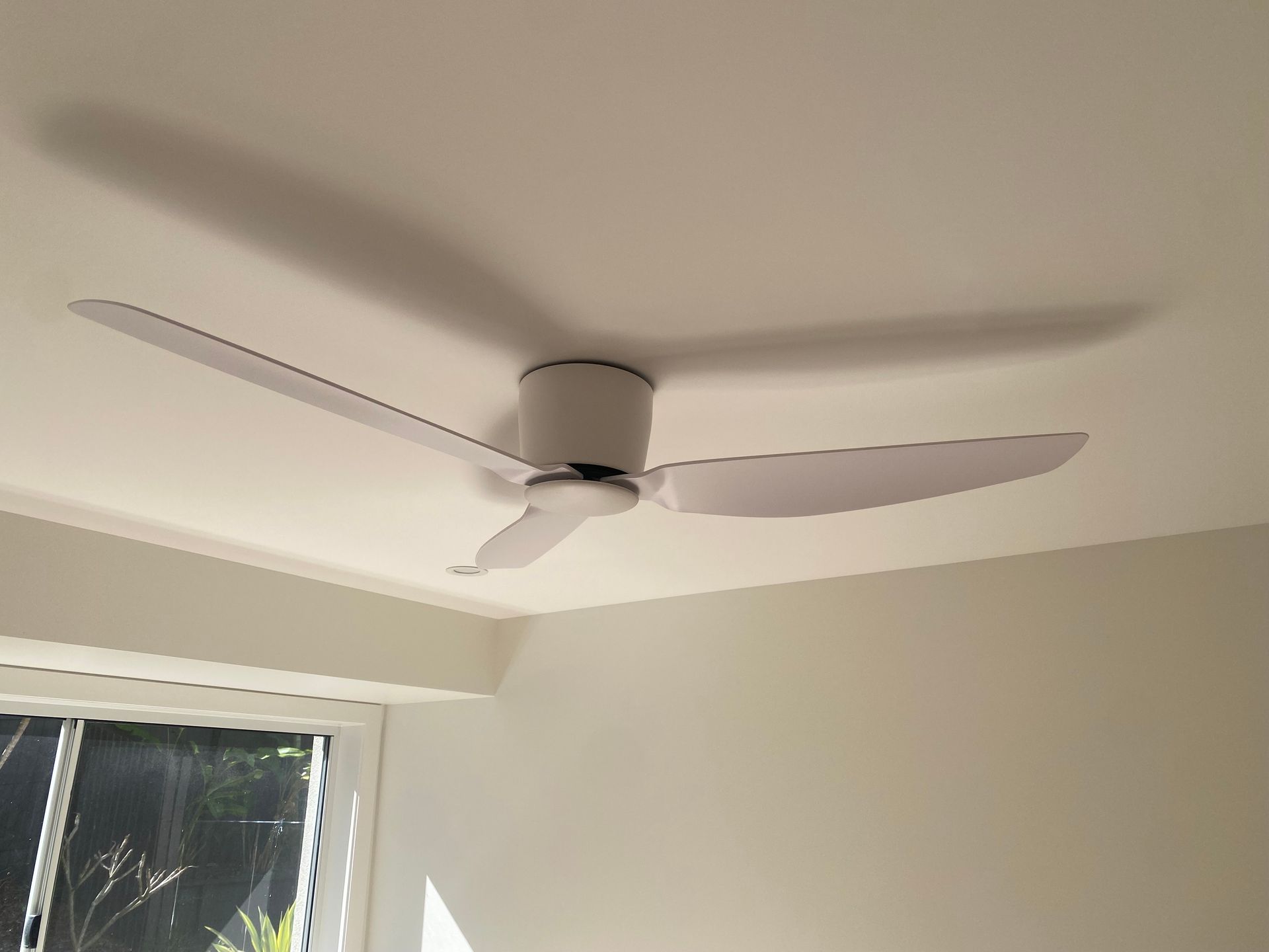 White ceiling fan with three blades mounted on a white ceiling casting a shadow on the ceiling.