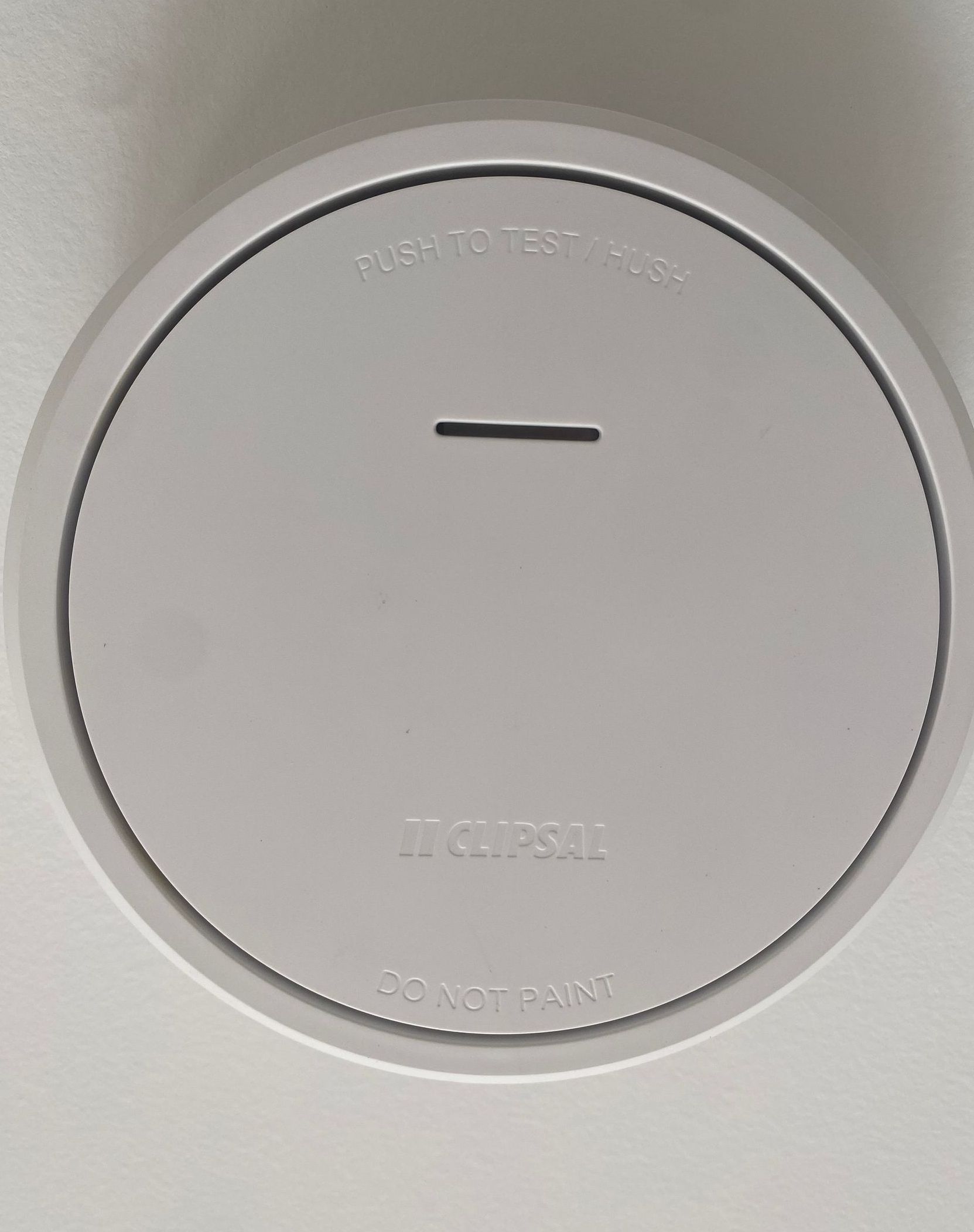 White smoke detector on a white ceiling, with a small slot in the center.