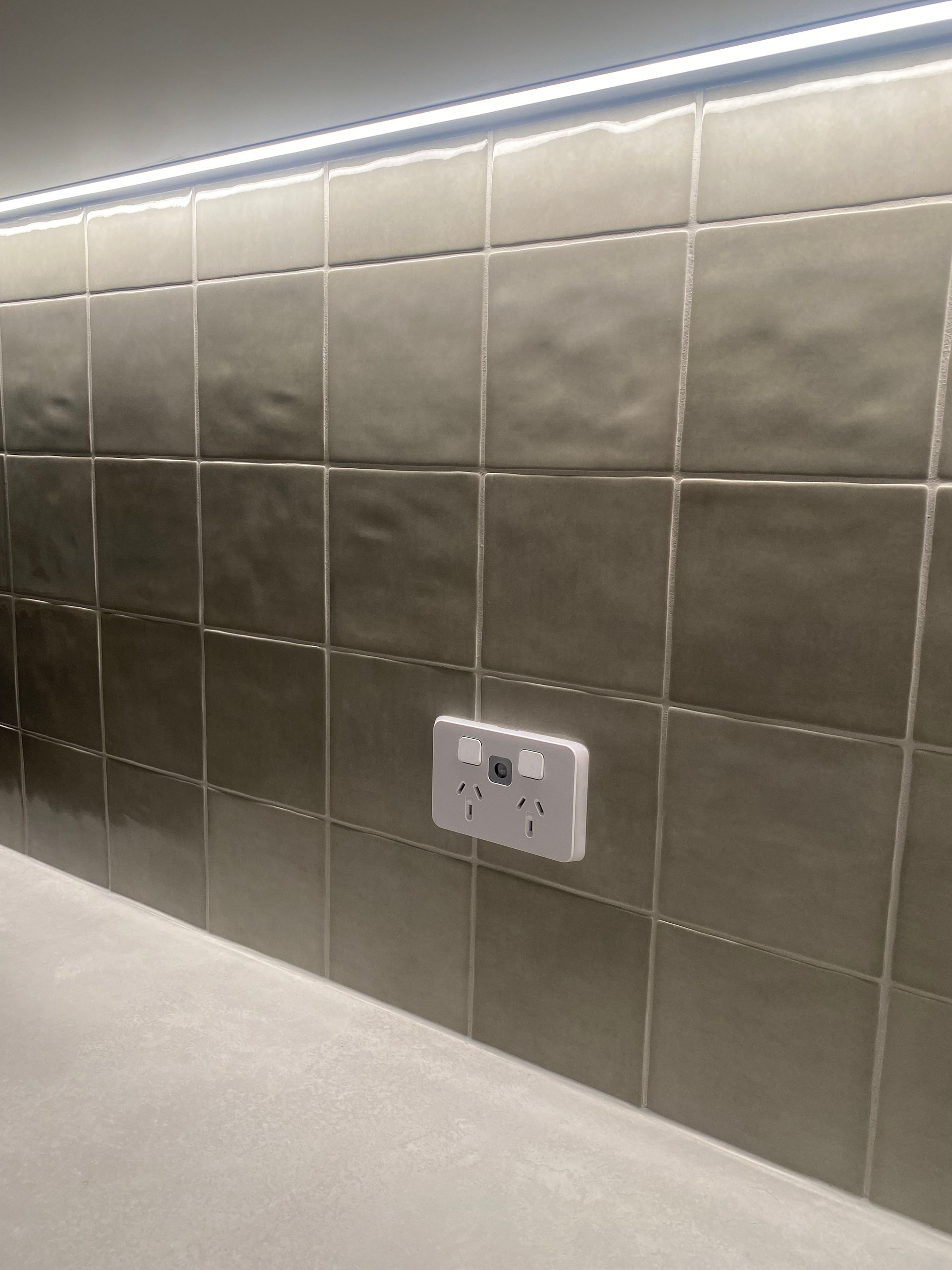 Gray tiled backsplash with a white electrical outlet. A strip light is above.