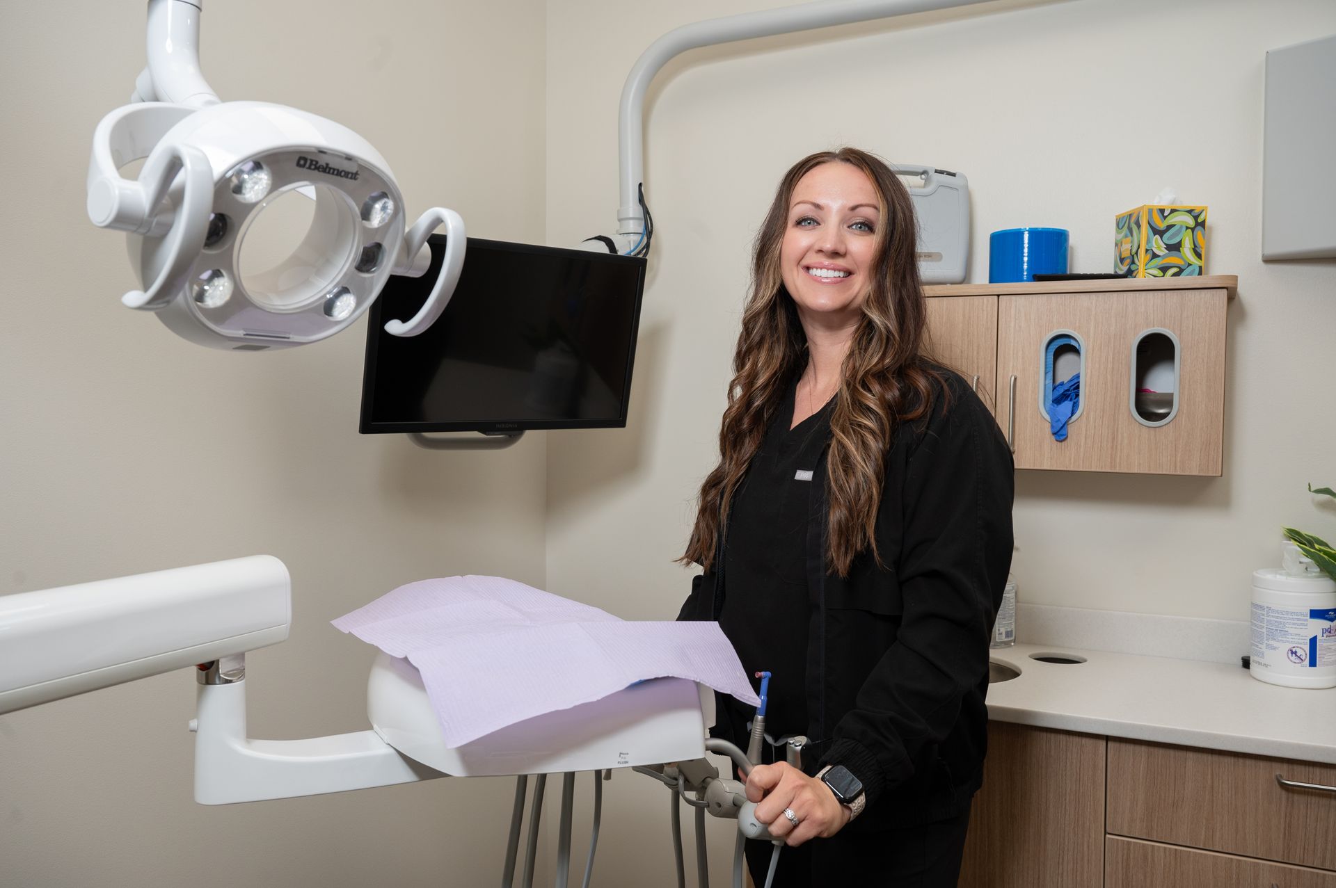 Dentist smiling in a dental office next to the patient's chair and tools.