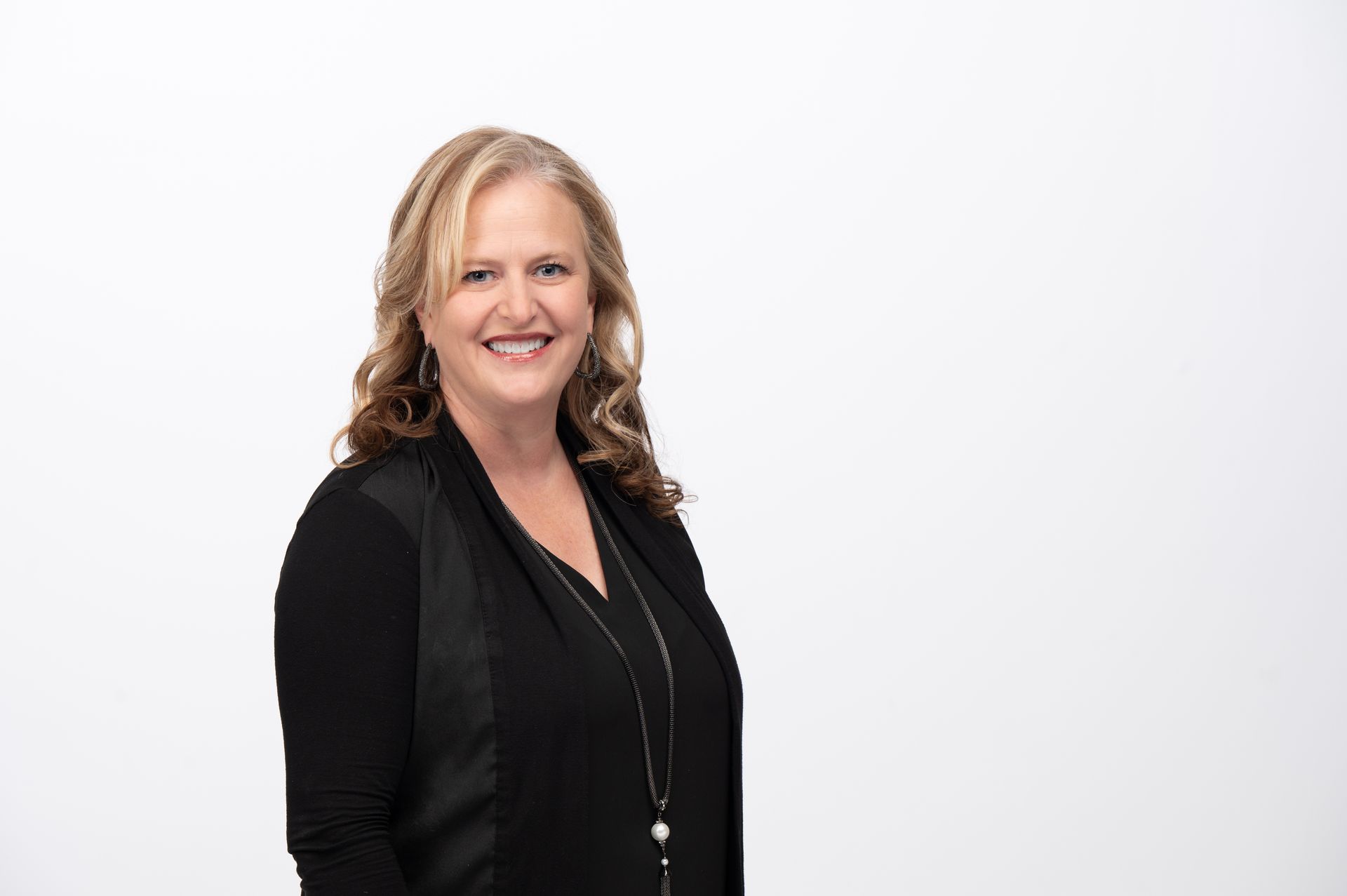 Woman with blond hair in black outfit smiles at the camera against a white backdrop.