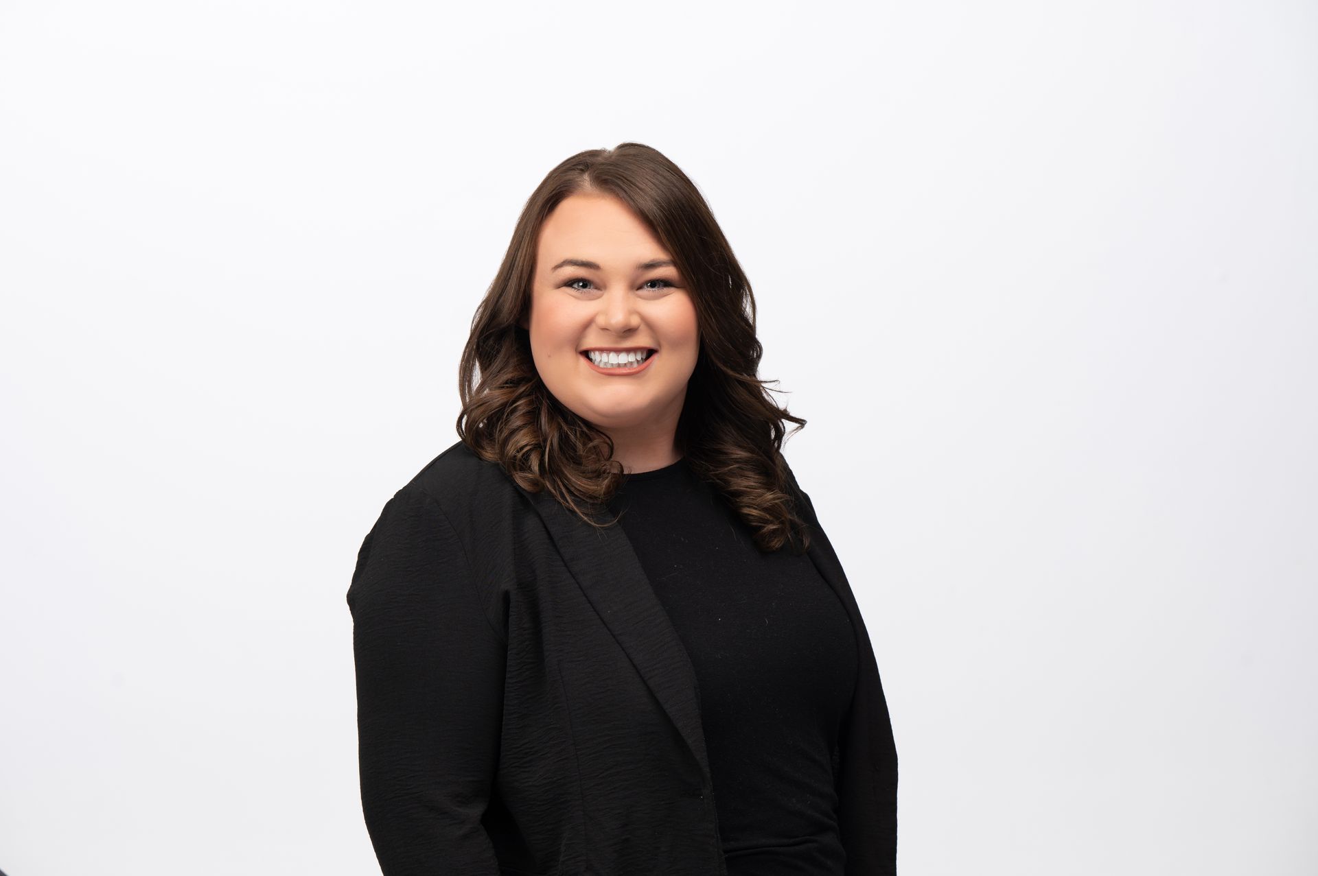 Woman in a black blazer smiling in front of a white background.