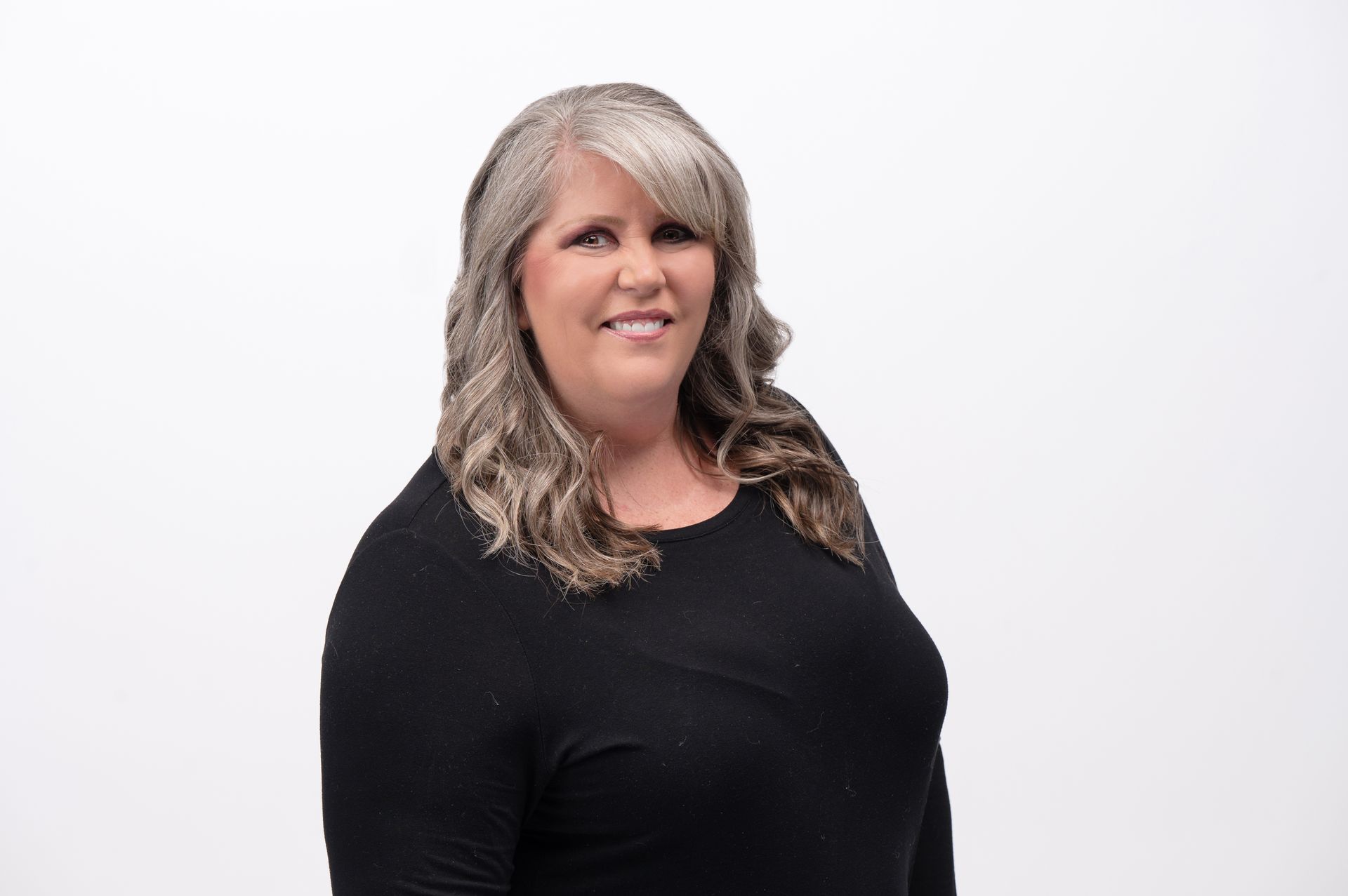 Woman with gray and brown hair smiles wearing a black long-sleeved shirt against a white background.