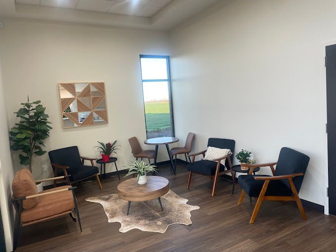 A waiting room with modern furniture, plants, and a window overlooking a field.