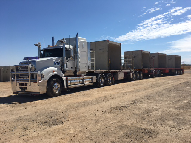 A silver semi-truck hauling four large grey containers on a flatbed trailer on a dirt road under a blue sky — Chewies Tipper Hire & Haulage in Gracemere, QLD