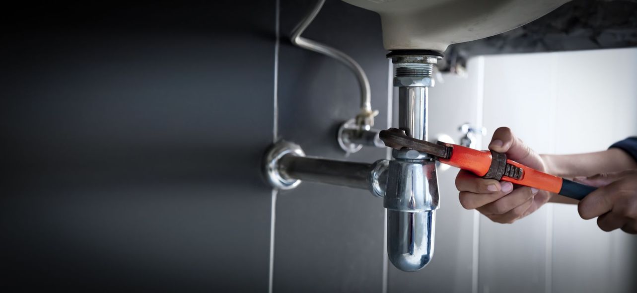 A plumber is fixing a sink pipe with a wrench.