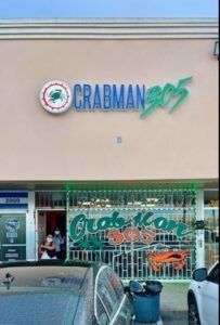 Crabman 305 restaurant exterior with green and blue neon sign, plus a car parked in front.