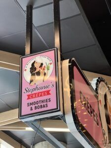 Sign for Stephanie's Crepes, Smoothies & Bobas; pink background with a woman, next to another Crepes sign.