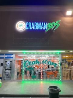 Crabman 305 restaurant exterior at night with neon green and blue signage and a security gate.