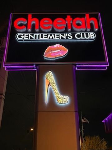 Sign for Cheetah Gentlemen's Club at night: red text, neon outline, a lip graphic, and high-heeled shoe graphic.