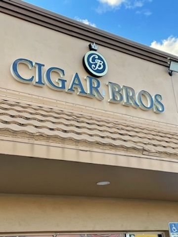 Sign for Cigar Bros store, silver lettering on tan building, blue sky backdrop.