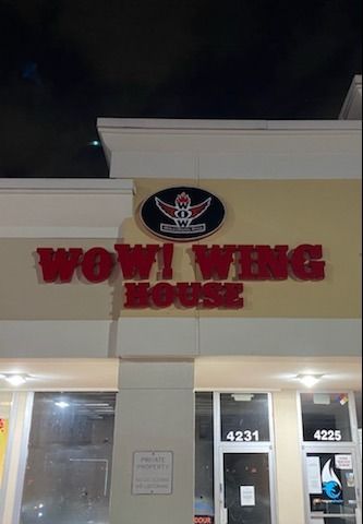 Wow! Wing House restaurant sign. Red letters on cream-colored building facade. Nighttime.