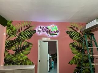 Pink wall with green palm leaves, neon sign above doorway, ladder.