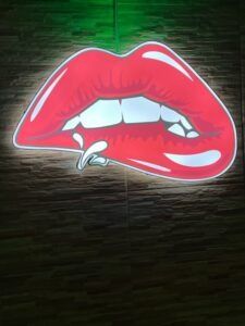 Red cartoon lips with a lip piercing, white teeth, and a wooden background.