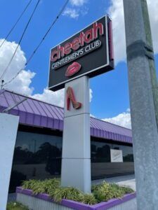 Sign for Cheetah Gentlemen's Club, with a red lip and shoe graphic, against a purple roof and blue sky.