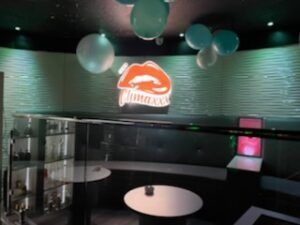 Interior of a bar, featuring a lip-shaped logo, balloons, and round tables.