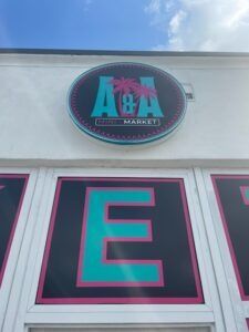 Sign for A&A Market: black background, turquoise and pink lettering, palm tree logo.