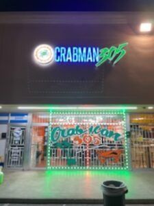 Crabman 305 restaurant exterior with neon sign and green trim.