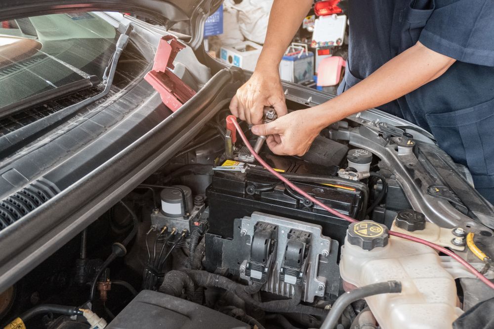 Mechanic Connecting Jumper Cables To A Car Battery In An Engine Bay — Britek Automotive in Bentley Park, QLD