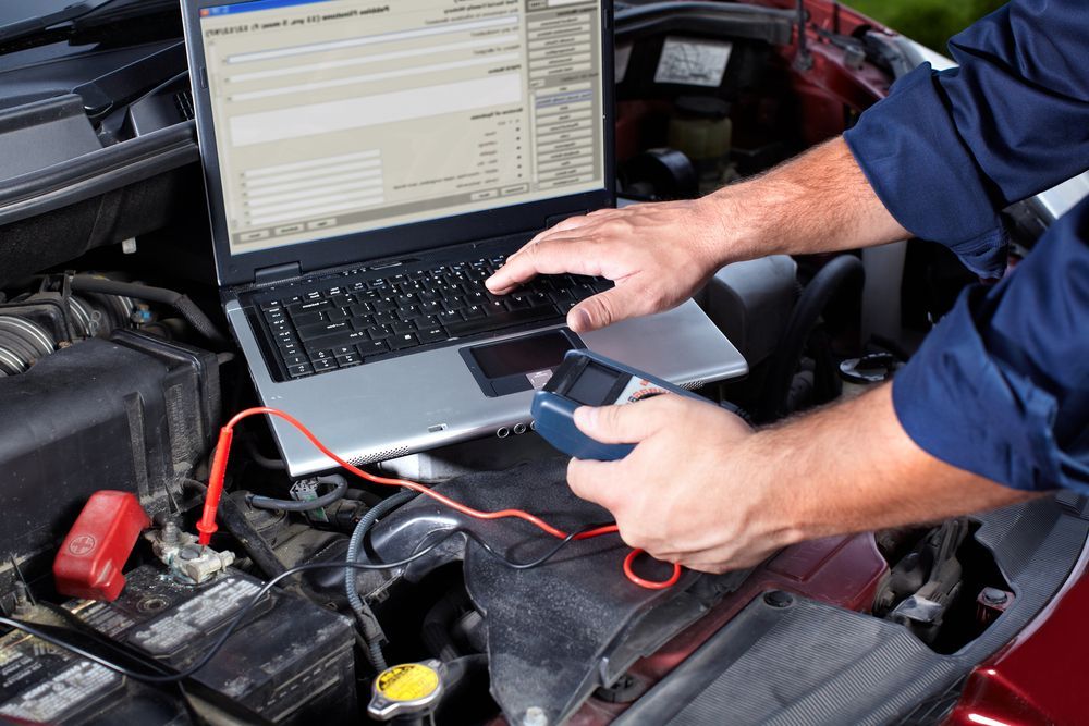 Mechanic Using A Laptop And Multimeter To Diagnose A Car Engine In A Garage — Britek Automotive in Bentley Park, QLD