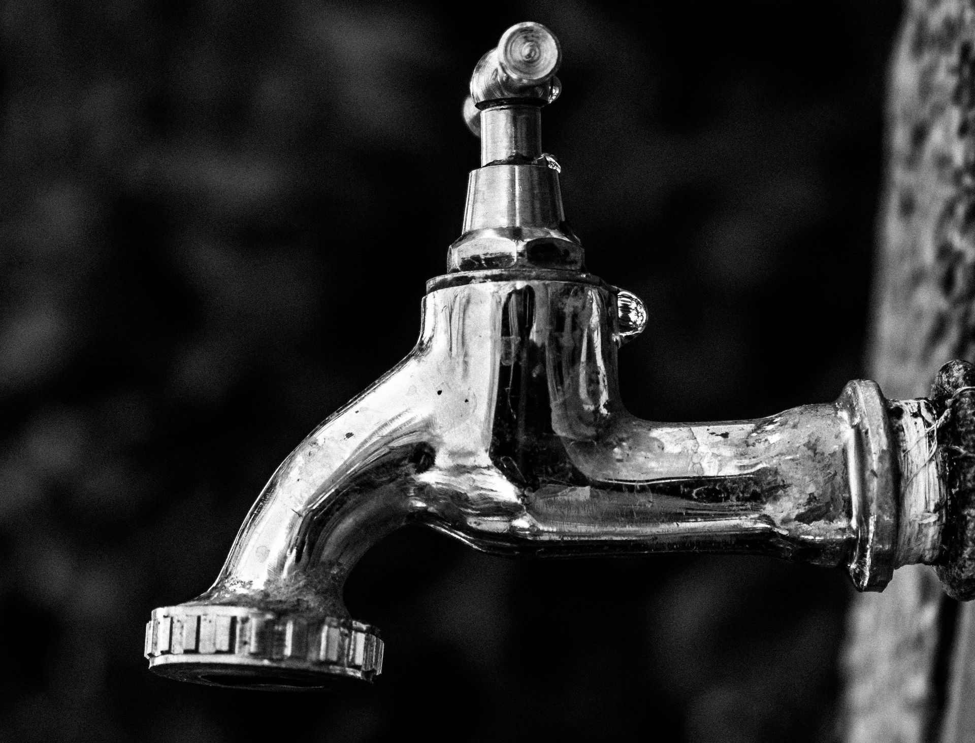 A black and white photo of a faucet on a wall.