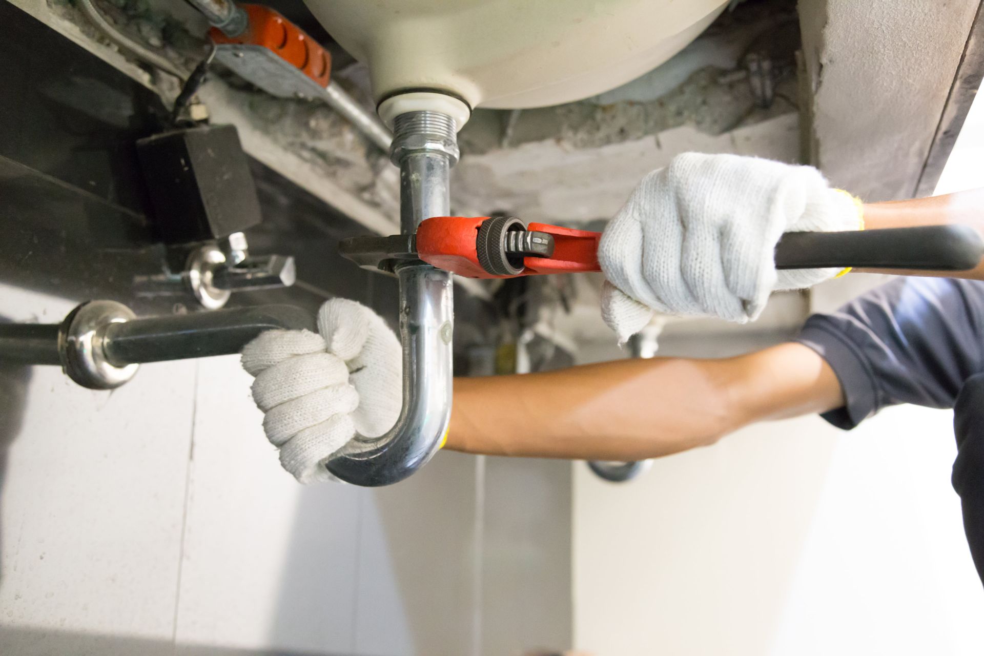 A plumber is fixing a sink pipe with a wrench.