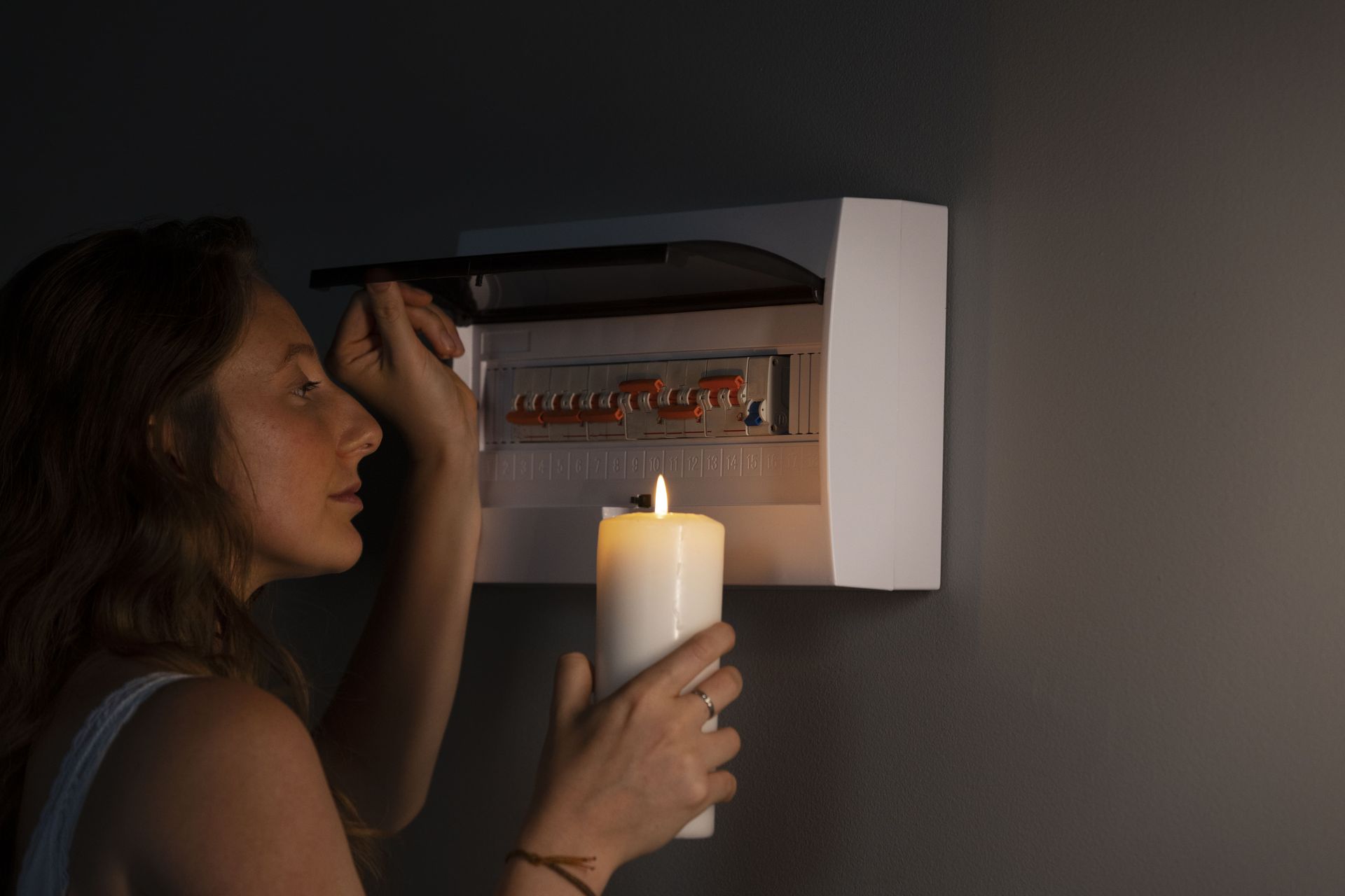 A woman is holding a candle in front of an electrical box.