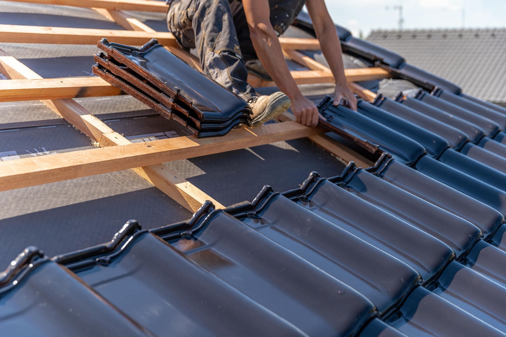 A man is laying tiles on the roof of a house.