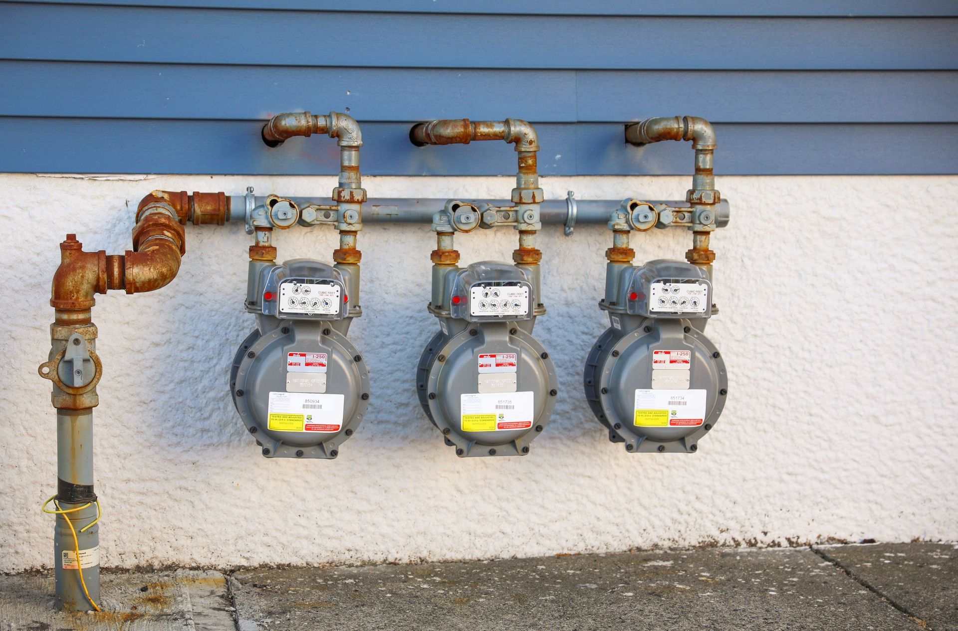 Three gas meters are connected to a pipe on the side of a building