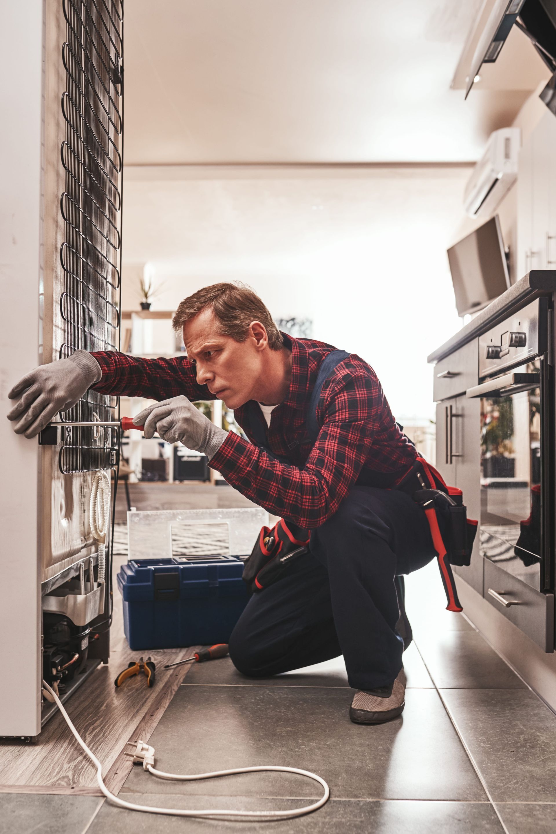 A man is working on a refrigerator in a kitchen.