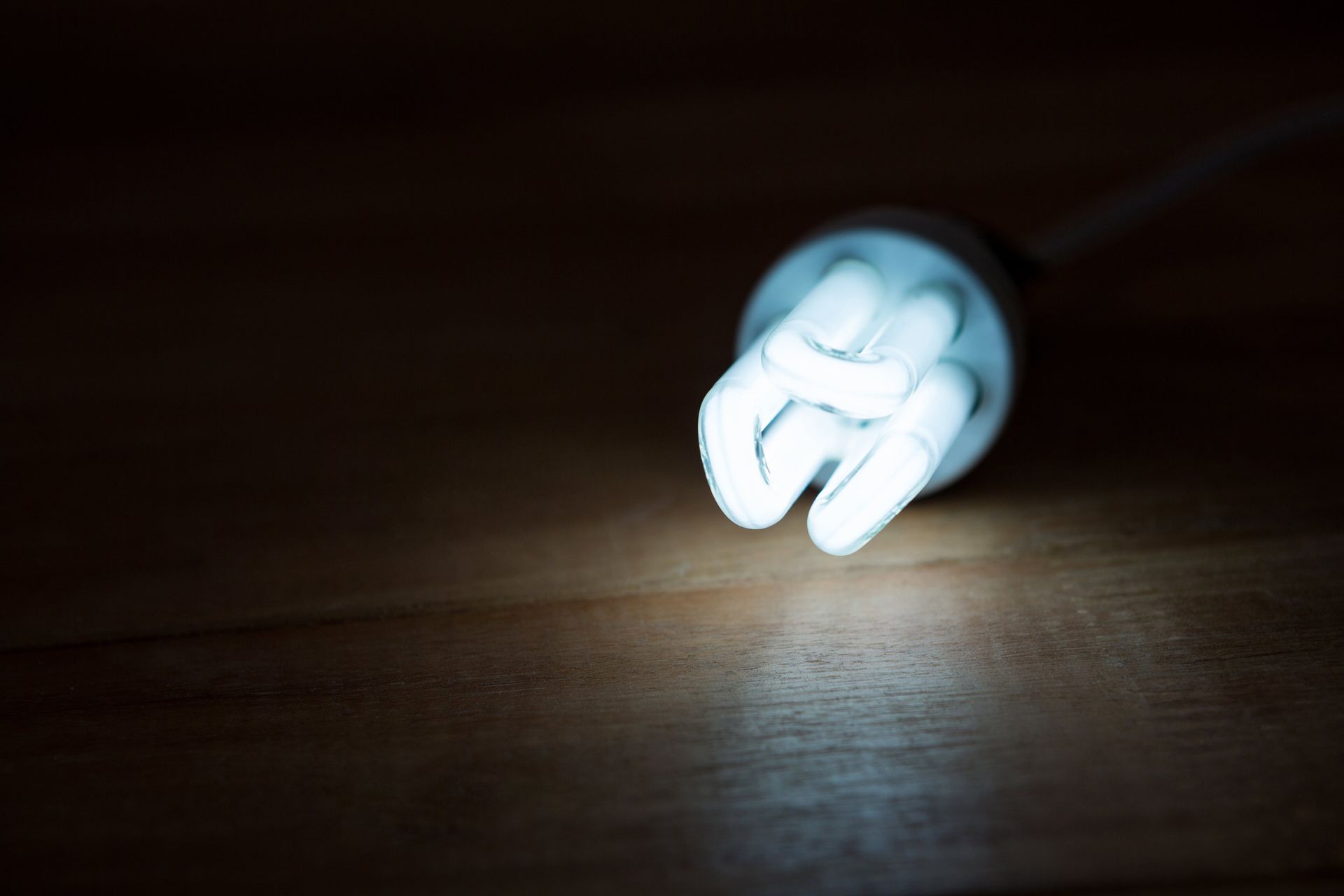 A light bulb is glowing in the dark on a wooden floor.