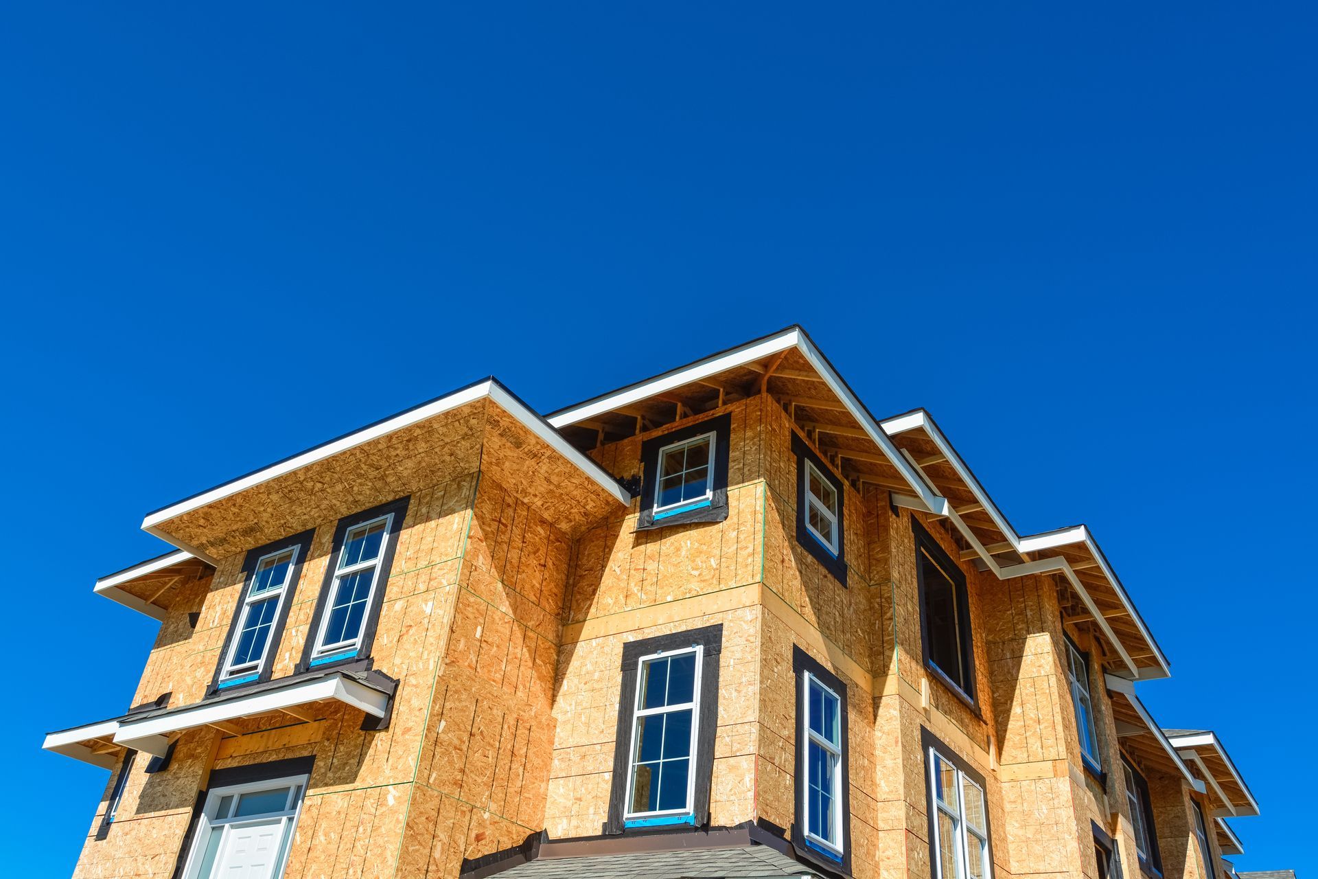 Multi-story building under construction, showing wooden frame, window frames, and bright blue sky.