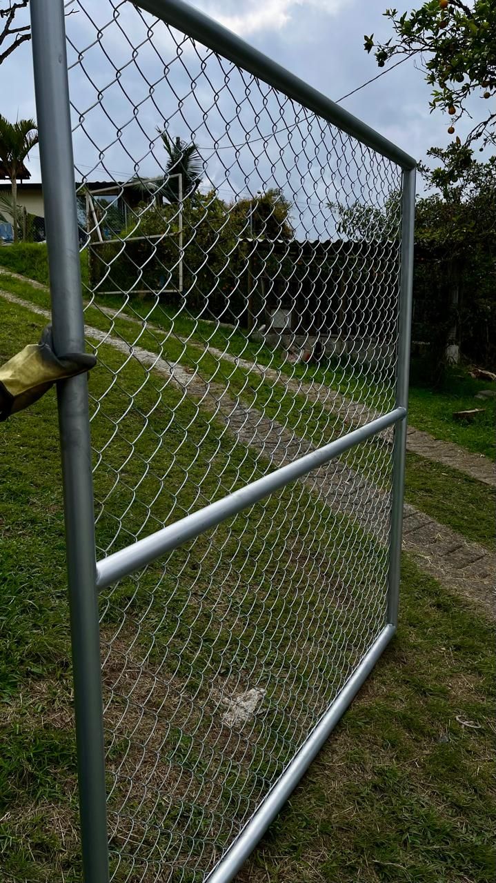 Una persona sostiene una valla de alambre de cadena en un campo.