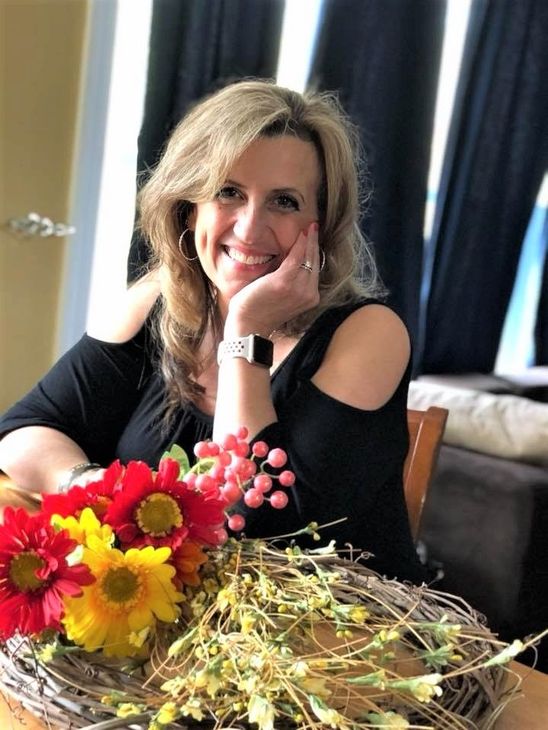 A woman is sitting at a desk with a laptop and a vase of flowers.