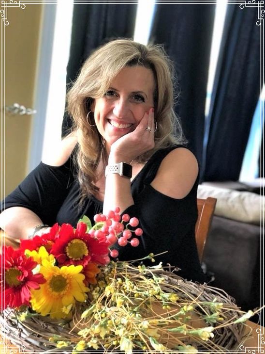 A woman is sitting at a desk with a laptop and a vase of flowers.