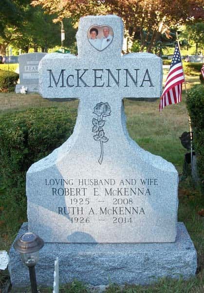 Gravestone for Robert and Ruth McKenna. Gray stone cross shape, photo of couple, US flag in background.