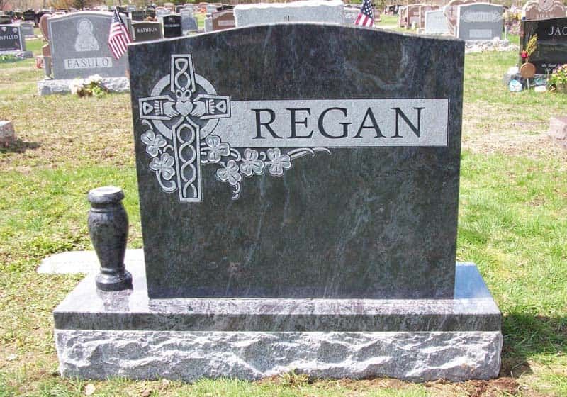 Dark gray Regan headstone with Celtic cross, urn, and light gray base, in a grassy cemetery.
