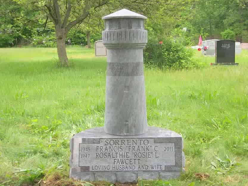 A grey lighthouse-shaped gravestone in a cemetery. 
