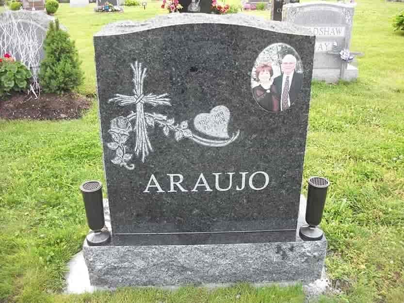 A dark granite headstone with engraved cross, flowers, heart, and family photo; 
