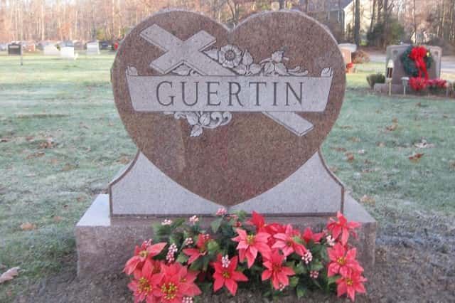 Heart-shaped Guertin tombstone in a cemetery, decorated with flowers; cross and scroll design.