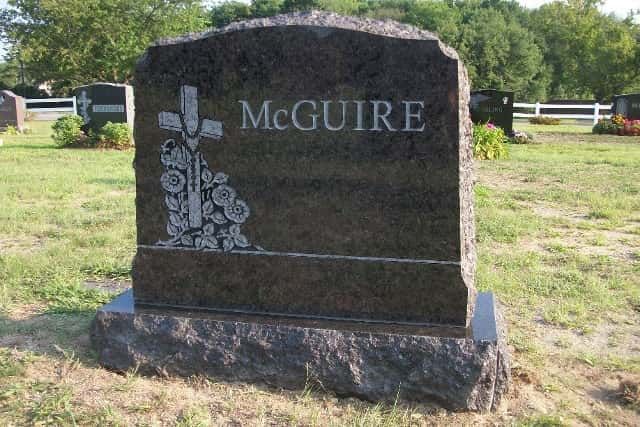 Dark granite McGuire headstone in a cemetery, with a cross and floral design.