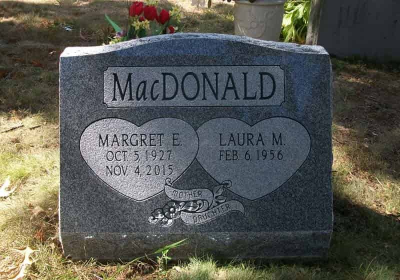 Gray granite headstone with the MacDonald surname, two hearts containing names and dates, set in a grassy cemetery.