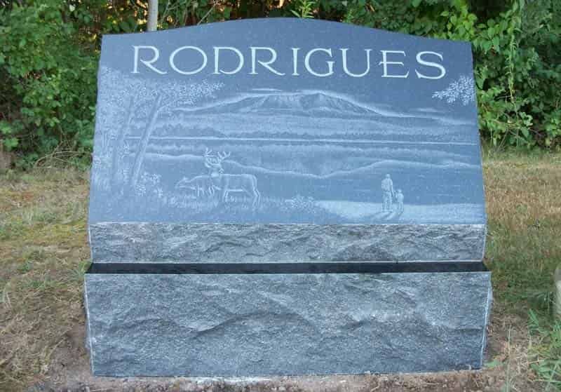 Dark gray granite headstone; engraved landscape scene with family, mountain, and water, RODRIGUES.