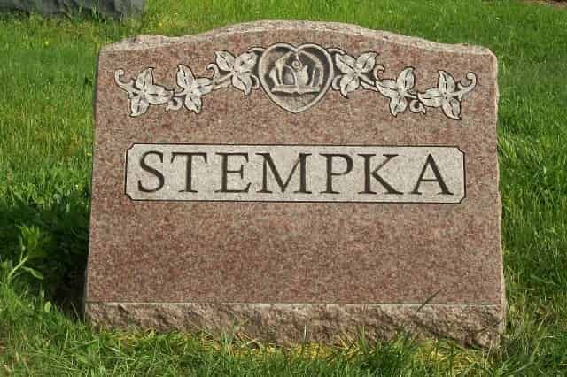 Gravestone with the name STEMPKA on a reddish-brown stone, with ivy-like design and a heart-shaped emblem.