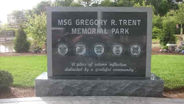 Memorial sign in a park: MSG Gregory R. Trent. Black granite, with military emblems, grassy setting.