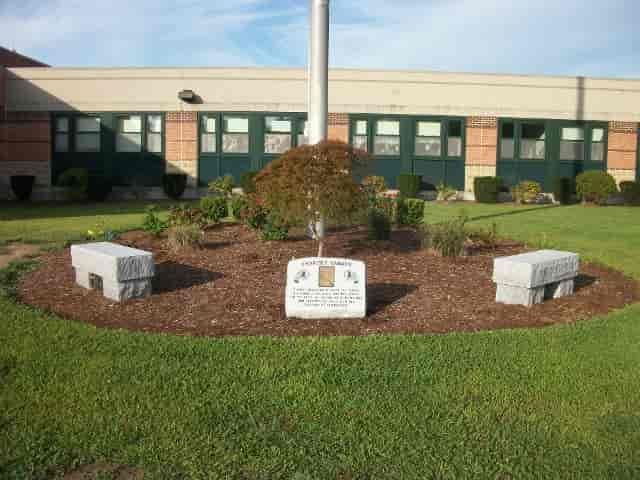 Flower bed with benches and a flagpole in front of a school building.