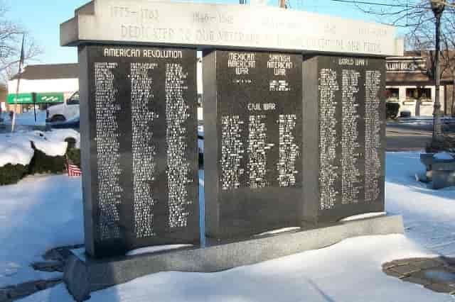 War memorial with names inscribed on black granite panels, set in a snowy area.