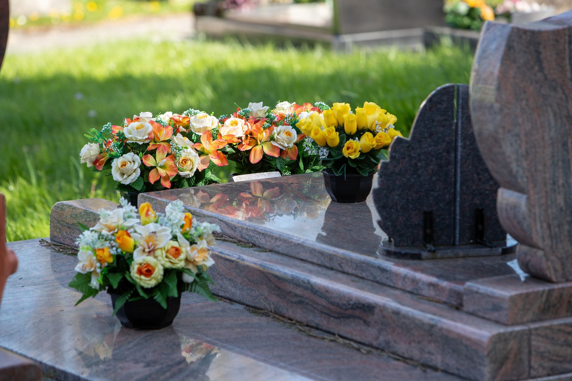 Polished granite gravestone adorned with colorful flower arrangements in a quiet cemetery setting.