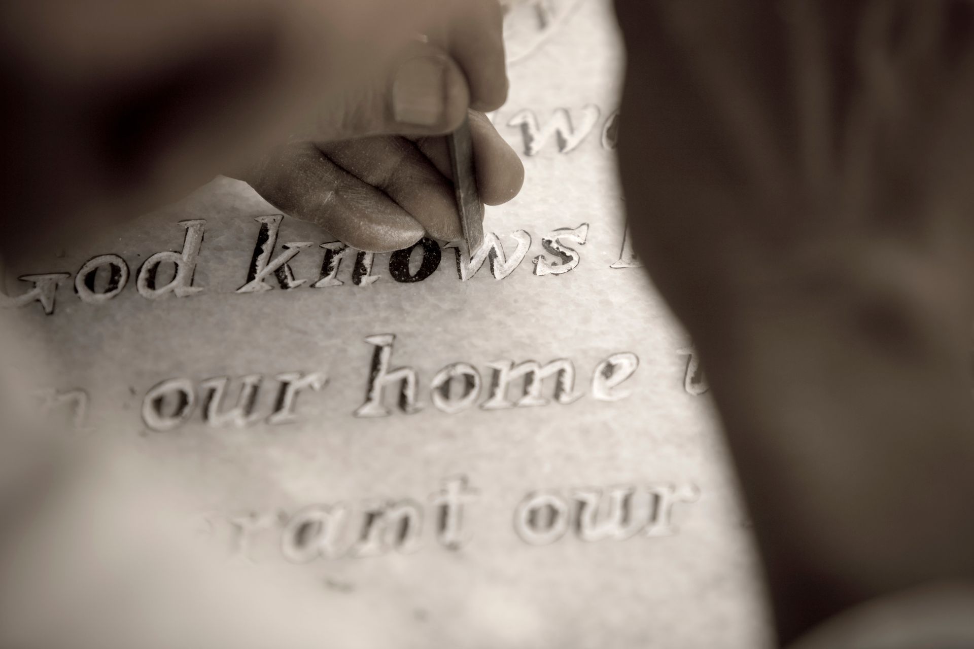Person using a tool to carve text into stone; close-up on hand, words 