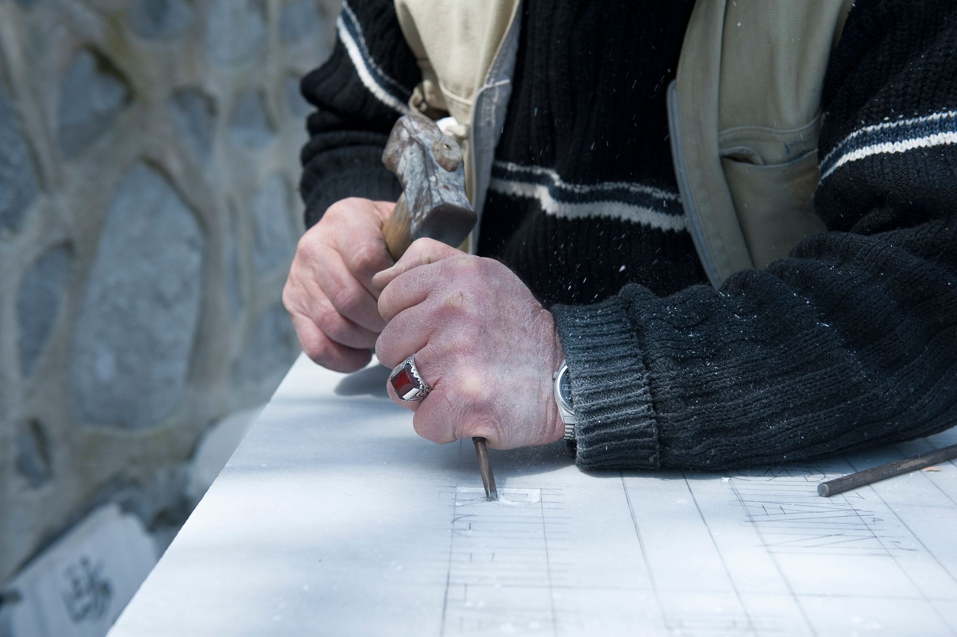 Sculptor chiseling a stone surface with a hammer and chisel, following a blueprint in a workshop.